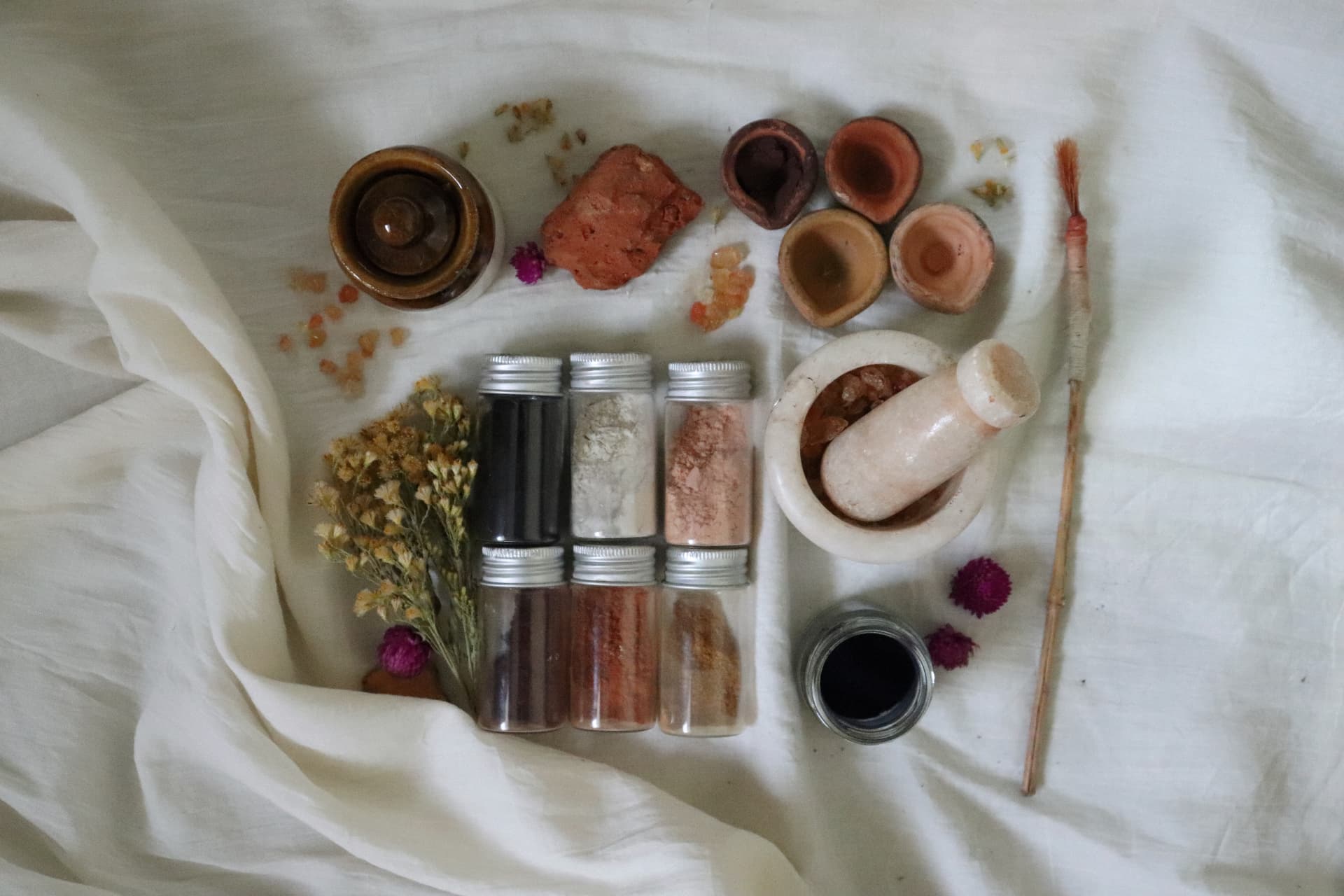 Earth pigments in glass vials, stone bowls and a marble mortar on white cloth